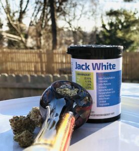 outdoor photo of buds of jack white strain pictured with a packed multi-colored glass bowl with a blue green and mostly white forwardgro container in the background
